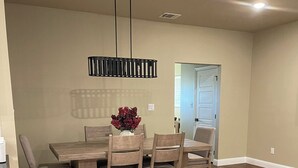 A dining area with a wooden table and chairs, a hanging light fixture, and a door in the background.