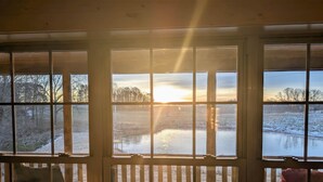 Huone, jossa on suuret ikkunat, joista avautuu näkymä jäiselle järvelle, sekä puinen terassi ja tuoli.
