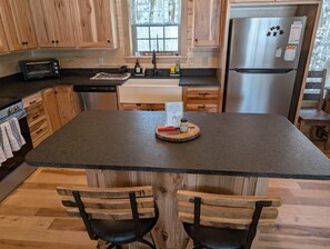 A kitchen with wooden cabinets, a stainless steel refrigerator, a toaster, and a wooden dining table with two chairs. - Willow Lane Cabins (McArthur)
