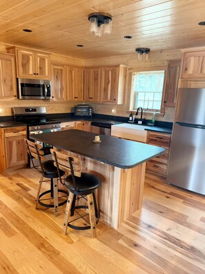 A kitchen with wooden cabinets, a stainless steel refrigerator, a microwave, a toaster, and a dining area with stools.