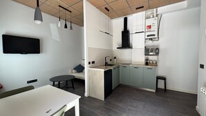 Eine kompakte Küche mit eingebauter Mikrowelle, Spüle und Herd. Es gibt einen Essbereich mit Tisch und Stühlen sowie einen an der Wand befestigten Flachbildfernseher.