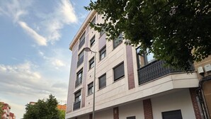 Ein mehrstöckiges Wohngebäude mit flacher Fassade, mehreren Balkonen und einem Parkplatz mit Autos.