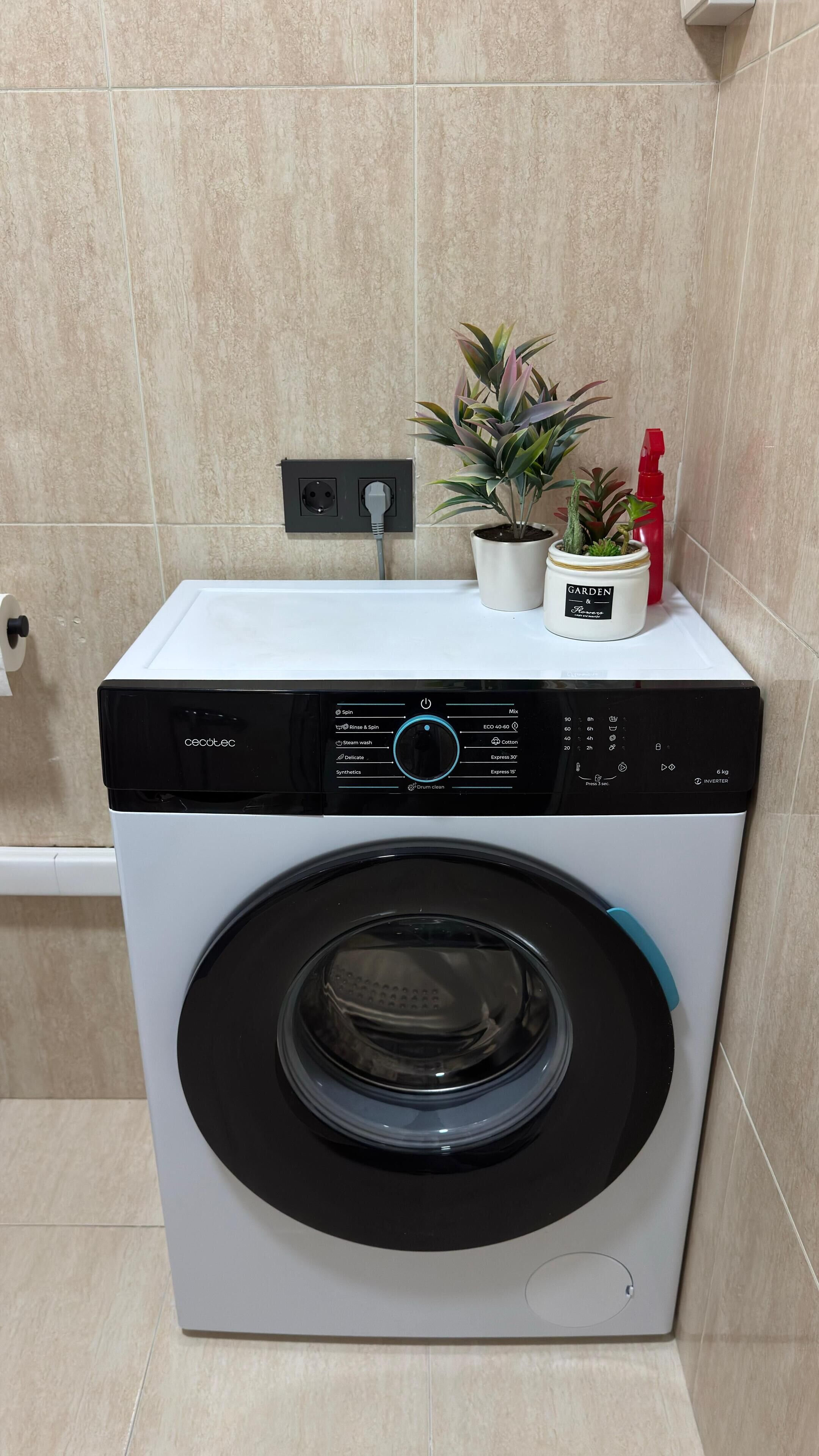 Una lavadora de carga frontal con un panel de control, un enchufe y una planta en la parte superior.
