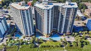 Un hôtel de grande hauteur doté de nombreux balcons, d’une piscine centrale et entouré de verdure.