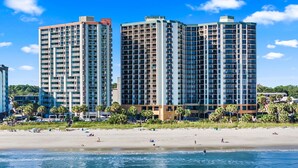 Un hôtel situé en bord de mer, composé de plusieurs immeubles de grande hauteur, avec une plage de sable et une vue sur l’océan.