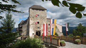 A historic stone building with a tower, surrounded by flags and greenery. - Becci`s Apartment- Free Parking (Kapfenberg)