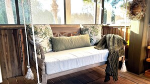 A wooden swing bed with a view of palm trees, a woven rug, and a hanging plant basket. - Affordable Waterfront Luxury!  "Jewel of Carrabelle" Perfect Condo on the Cove! (Carrabelle)