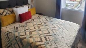 A bedroom with a bed, a painting, a window, and a view of the outside.