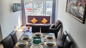 A dining area with a table set for six, a sofa with cushions, a clock, and a painting on the wall.