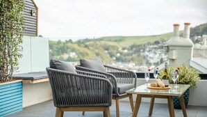 A terrace with two grey wicker chairs, a glass table with a bottle and glasses, and a view of a town. - Luxury Riverside Retreat in Dartmouth with views (Dartmouth)