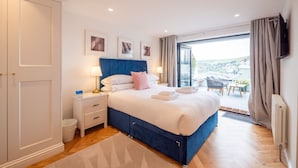 A bedroom with a large bed, a nightstand, a chair, and a view of the city through a balcony. - Luxury Riverside Retreat in Dartmouth with views (Dartmouth)