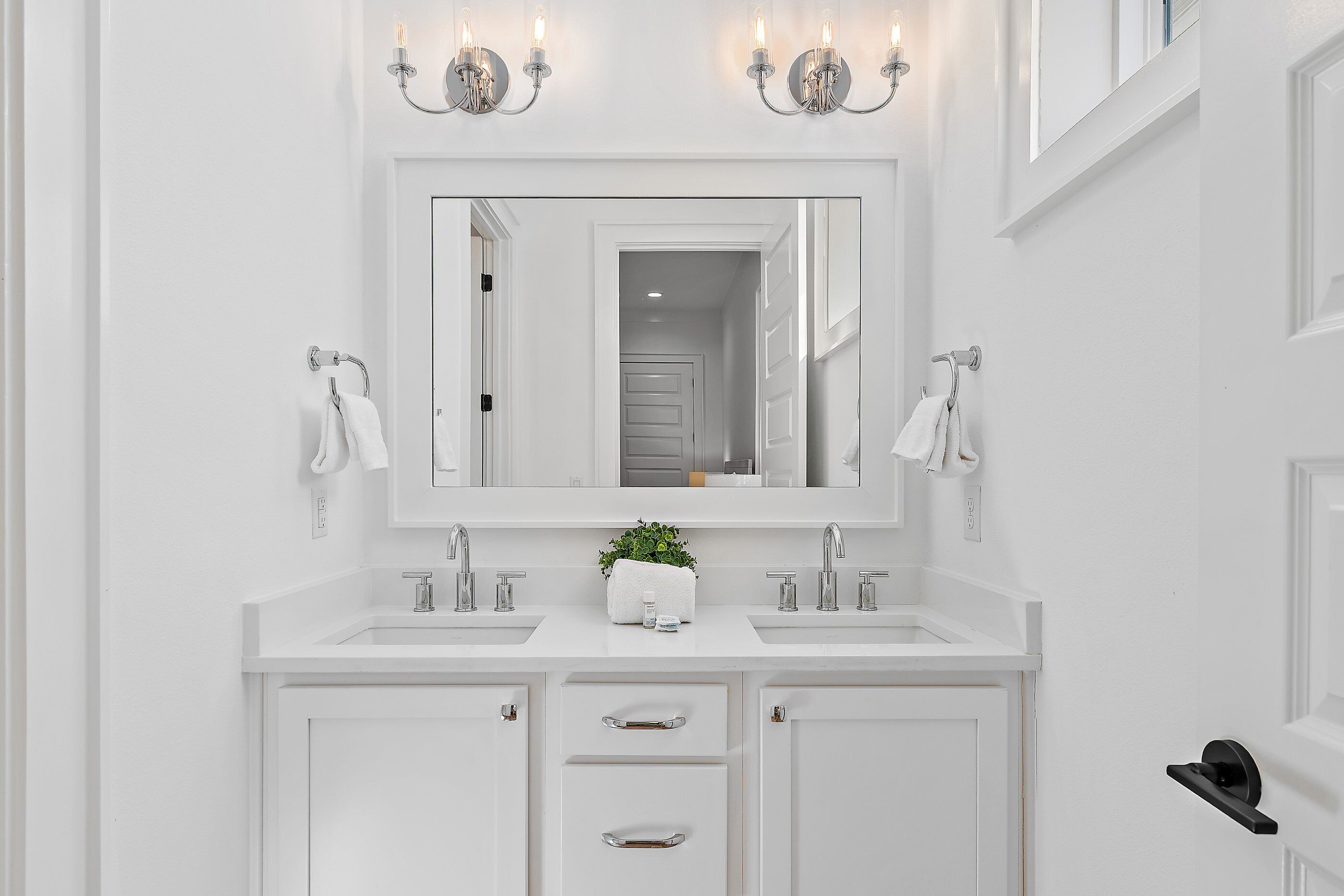 A white bathroom with two sinks, a large mirror, and a potted plant.