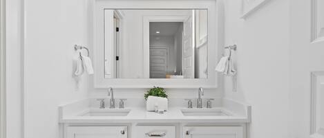 A white bathroom with two sinks, a large mirror, and a potted plant.