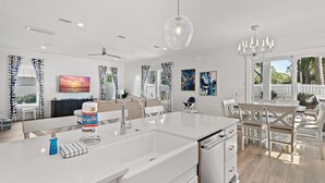 A modern kitchen with a large island, white cabinetry, and a dining area with white chairs and a table. - 🏖️Luxury 6BR-Private Pool-Scattered, Smothered, & Covered🏖️ (Miramar Beach)