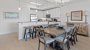 Une cuisine moderne avec des meubles blancs, un îlot central et un coin repas comprenant des chaises en bois et une grande table.