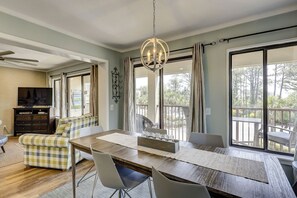 A dining area with a wooden table, chairs, a chandelier, and a view of the outdoors through large windows.