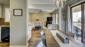 A modern living room with a sofa, a dining table with candles, and a large window with a view. - Coastal Escape w/ Pool & Ocean Peek! (Hilton Head Island)