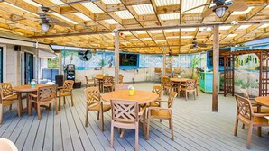 An outdoor patio with wooden tables and chairs, ceiling fans, and a mural on the wall. - Coastal Escape w/ Pool & Ocean Peek! (Hilton Head Island)