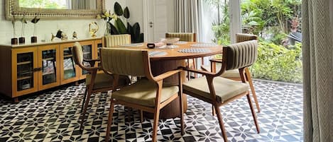 A dining area with a geometric patterned floor, a wooden dining table with chairs, a cabinet with glass doors, and a large mirror above the table.