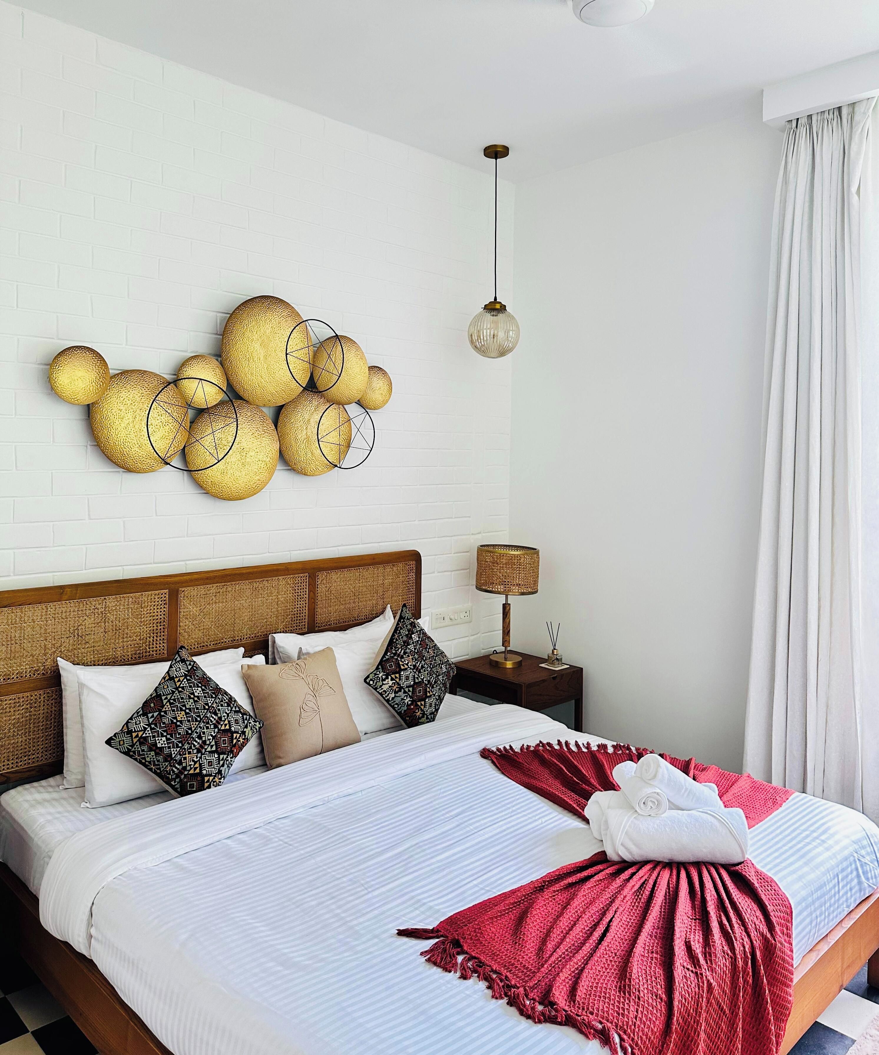 A hotel room with a bed, a wall-mounted decorative item, a hanging light fixture, and a nightstand with a lamp.