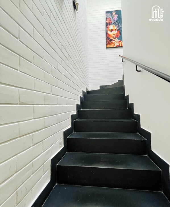 A staircase with white brick walls and black steps, leading to a room with a decorative painting. - Casa Calma by evaddo stays (Siolim)