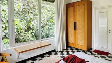 A hotel room with a bed, a bench, a wardrobe, and a window with a view of greenery.