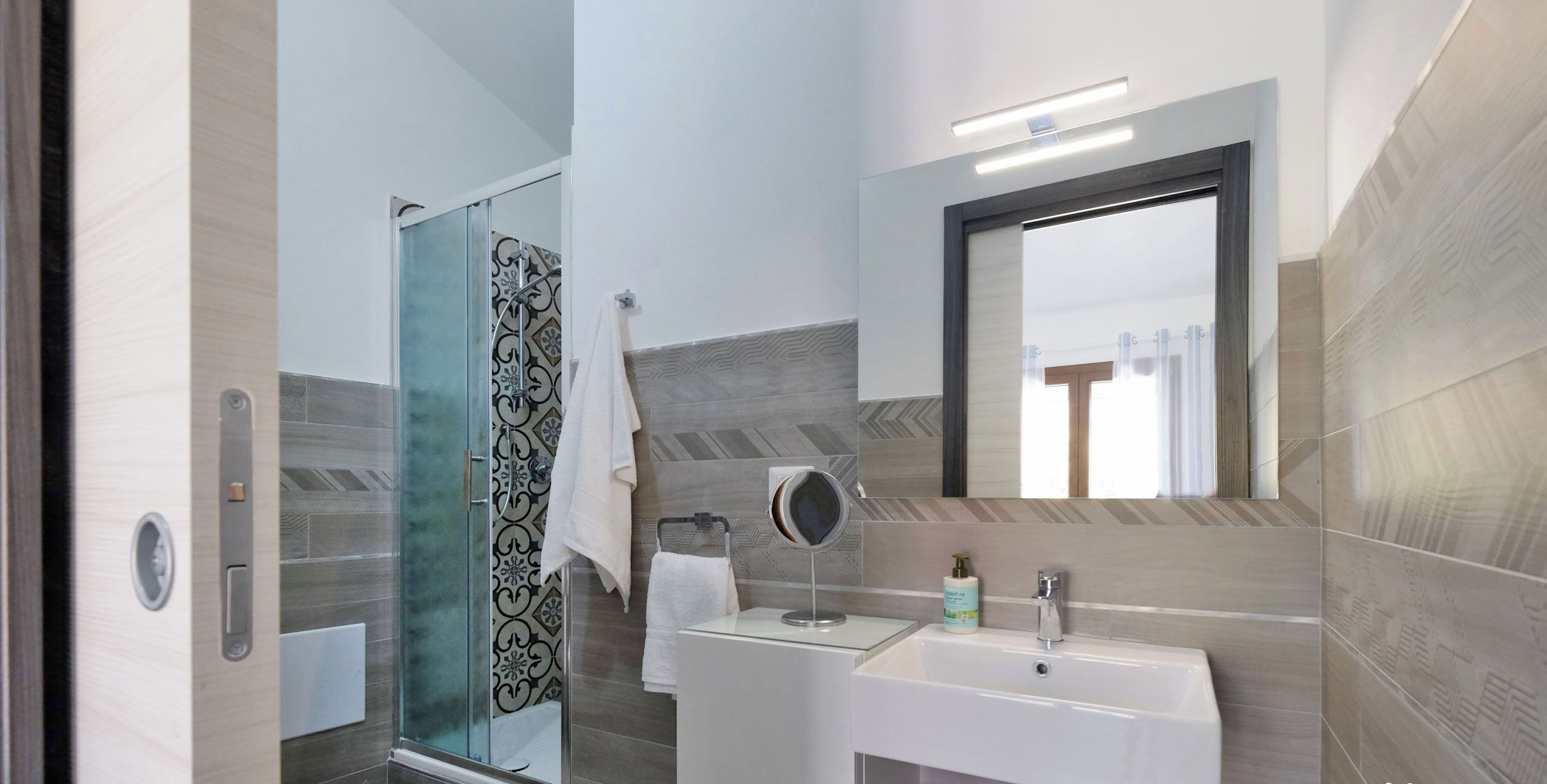 Un baño moderno con cabina de ducha de vidrio, un lavabo blanco y un espejo.