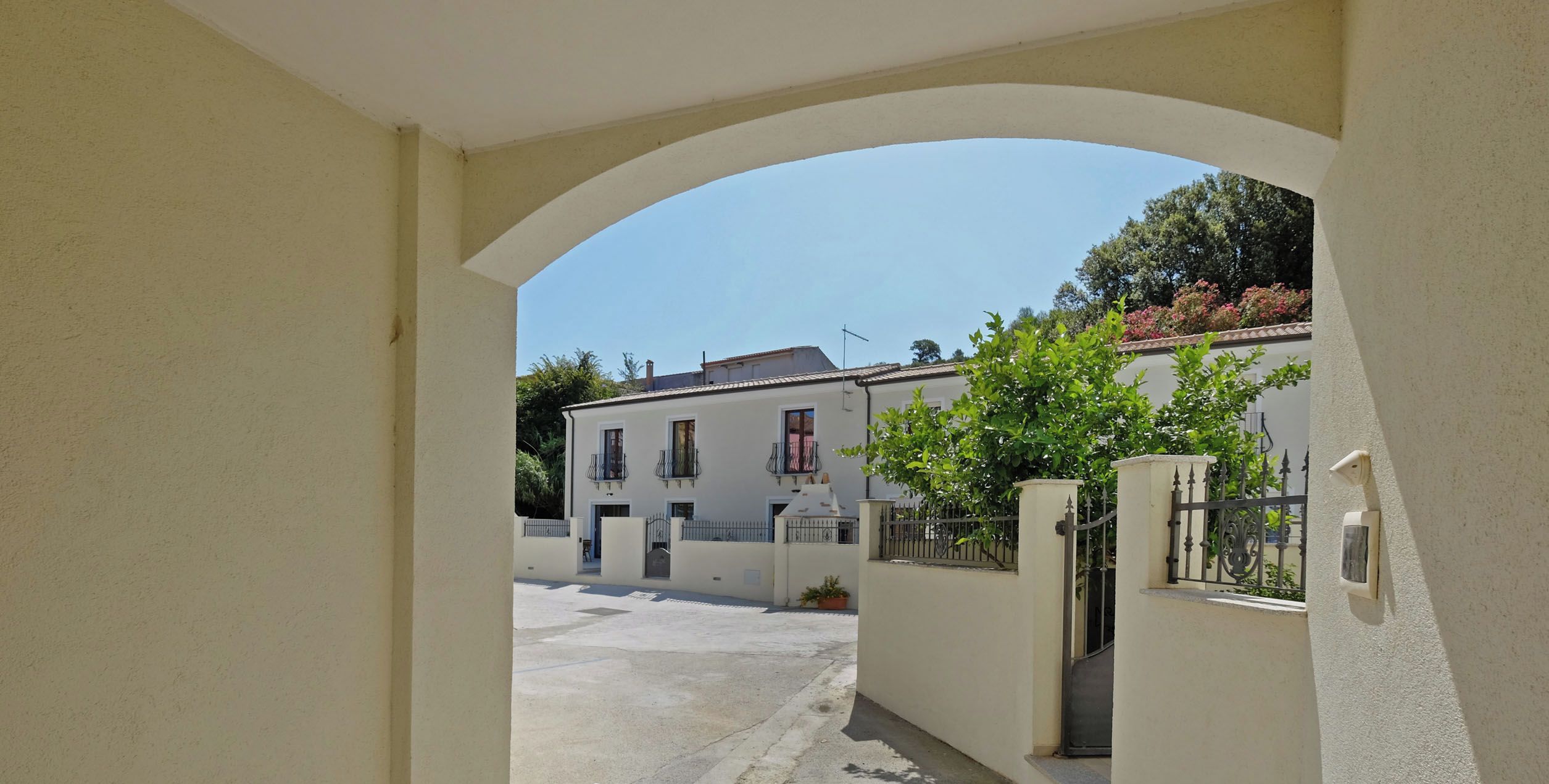 Un estrecho sendero que lleva a un edificio de fachada blanca, con un balcón y una puerta.