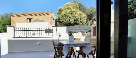 Un patio exterior con una mesa y sillas, una planta en maceta y vistas a un edificio y árboles.