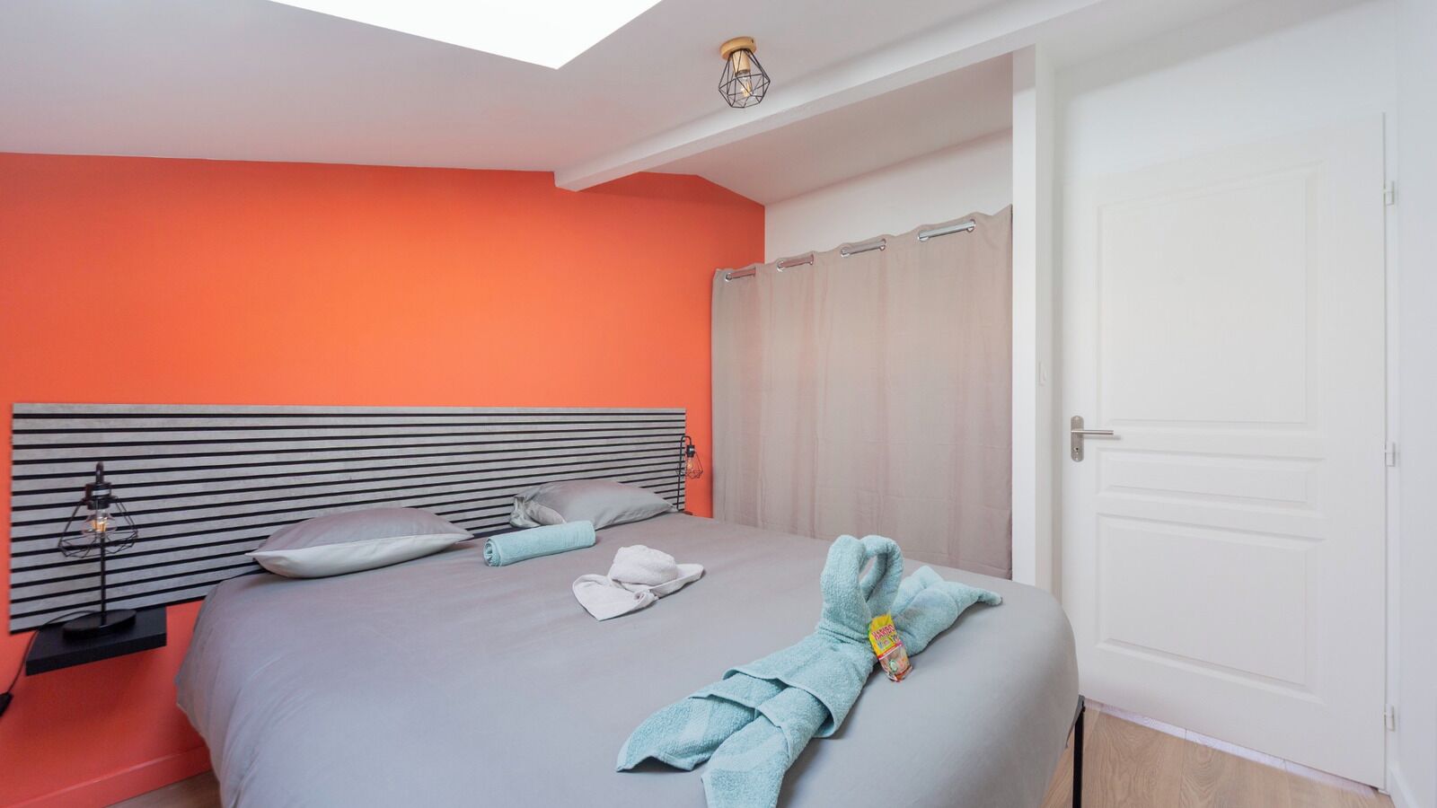 A modern bedroom with a bed, a bedside table, a nightstand, a window with curtains, and a door.
