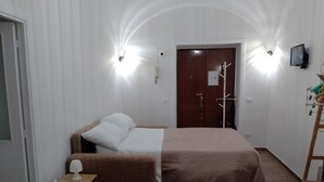 A room with a bed, a bedside table with a lamp, a wardrobe, and a TV mounted on the wall.
