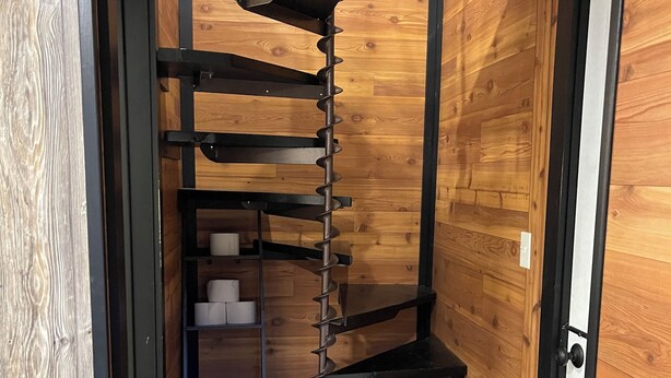 Een smalle inbouwkast met houten lambrisering, meerdere planken en een spiltrap.