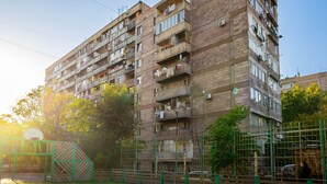 A multi-story residential building with balconies, a basketball court, and a green fence. - Apartment by Luxe Group XO444 (Yerevan)