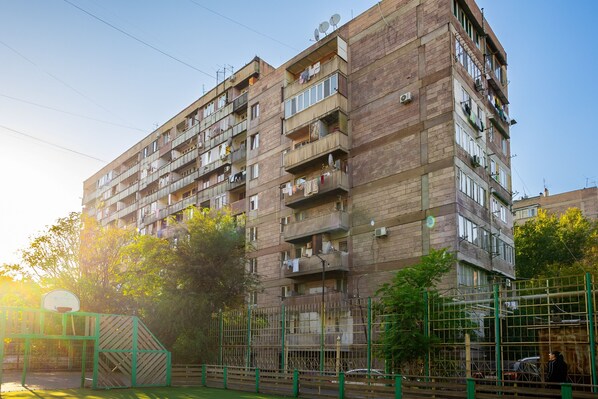 Un edifici residencial de diversos pisos amb balcons, una pista de bàsquet i una tanca verda.
