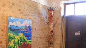 A room with a stone wall, a wooden bench, a colorful totem, and a painting of a landscape. - Large Art Nouveau house between sea and garrigue, charm and leisure in the heart of the South of France (Gabian)