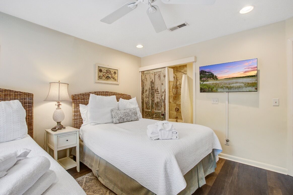 A bedroom with two beds, a ceiling fan, a painting, and a view of a landscape.