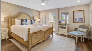 A bedroom with a wooden bed, a nightstand, a chair, and a television. - Seabrook Exclusives | 1203 Creekwatch (Seabrook Island)