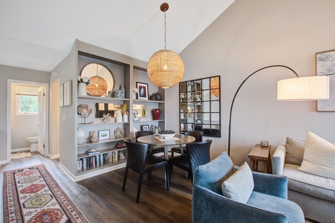 Un salon moderne avec une table à manger ronde, des chaises à l’assise rembourrée de couleur sombre, un canapé bleu et un grand luminaire suspendu en forme de lanterne.