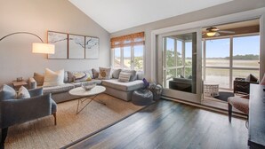 A spacious living room with a large window, a sofa set, a coffee table, and a floor lamp. - Seabrook Exclusives | 1203 Creekwatch (Seabrook Island)