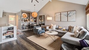 A spacious living room with a high ceiling, a large sofa, a coffee table, and a bookshelf. - Seabrook Exclusives | 1203 Creekwatch (Seabrook Island)