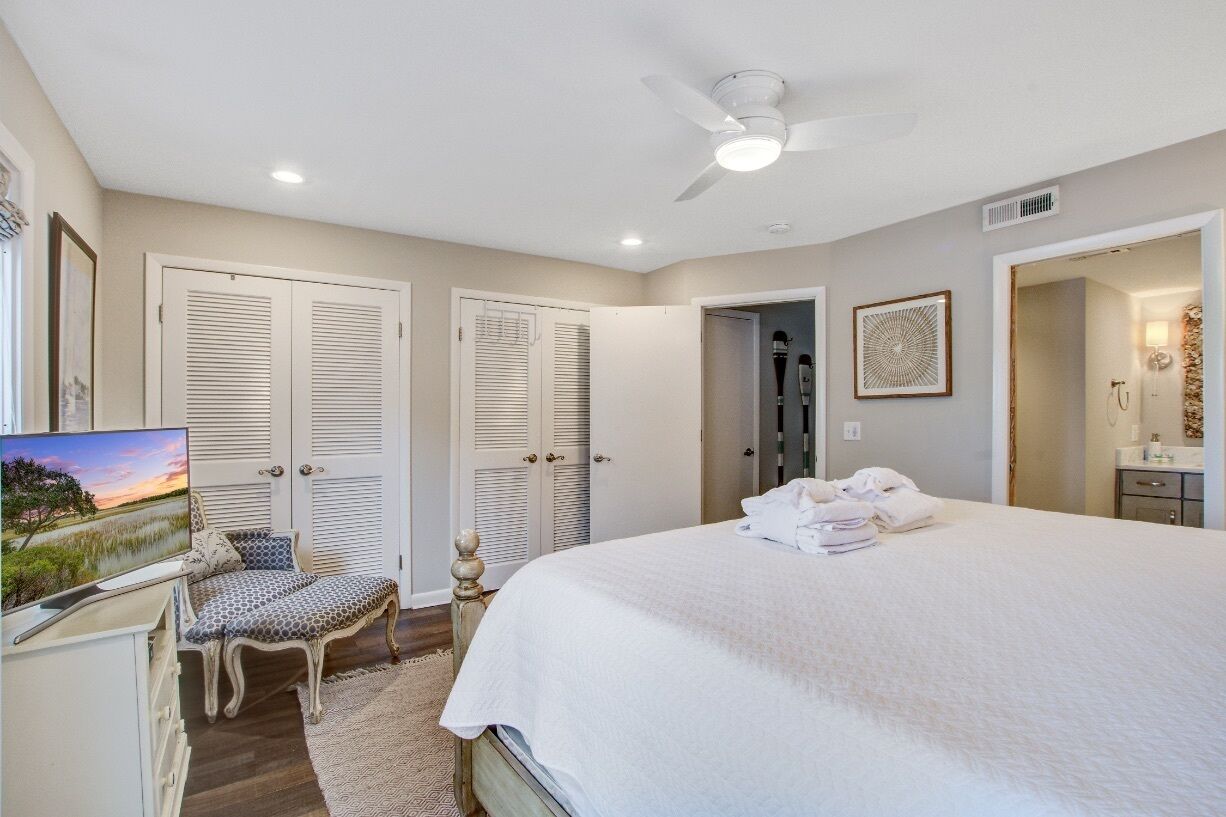 A bedroom with a bed, a TV, a chair, and a ceiling fan.