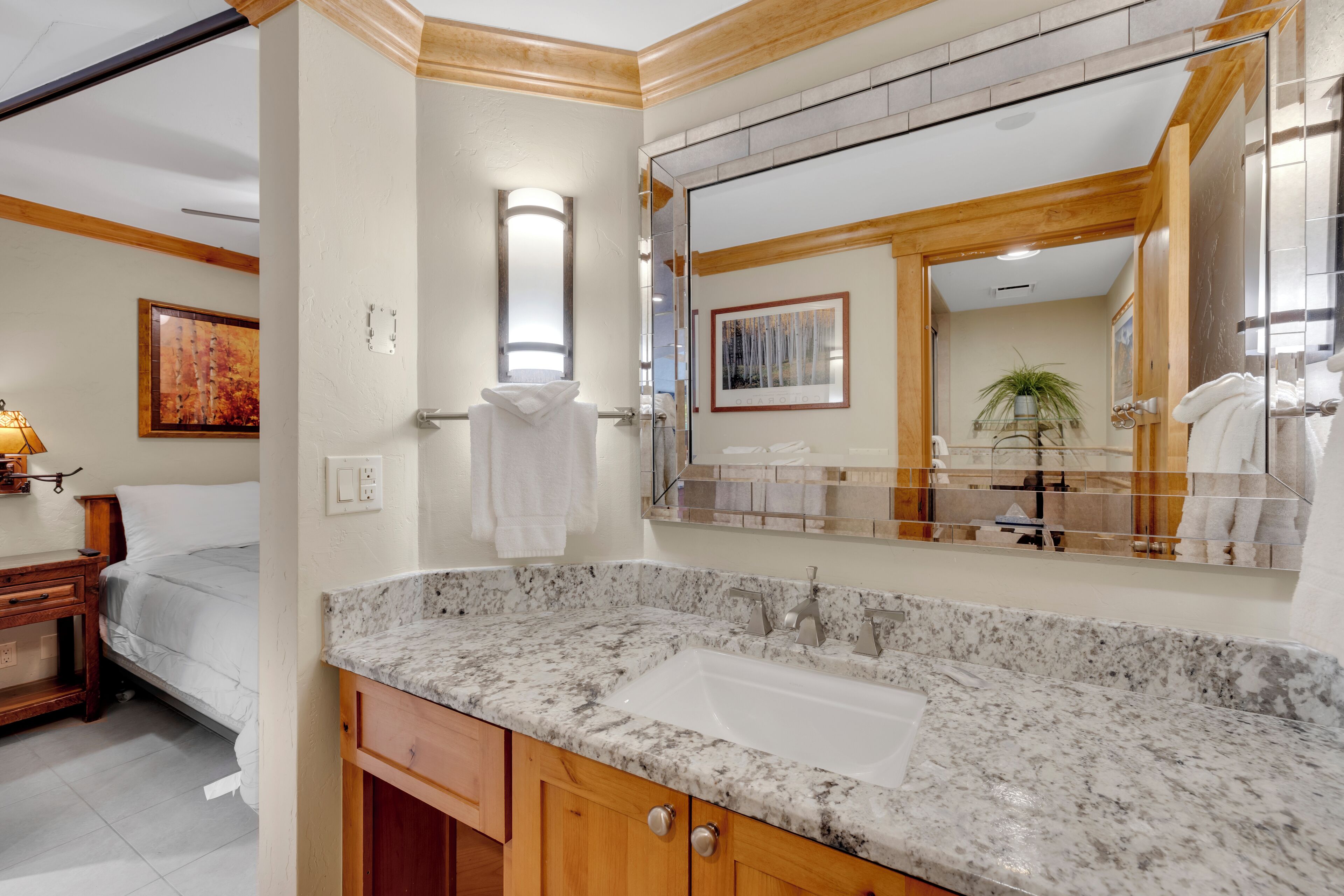 Une salle de bain avec un lavabo en marbre, des meubles en bois, un grand miroir et un lit avec une serviette blanche.