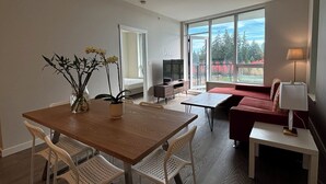 Moderni olohuone, jossa on puinen ruokapöytä, valkoiset tuolit, punainen sohva ja televisio.