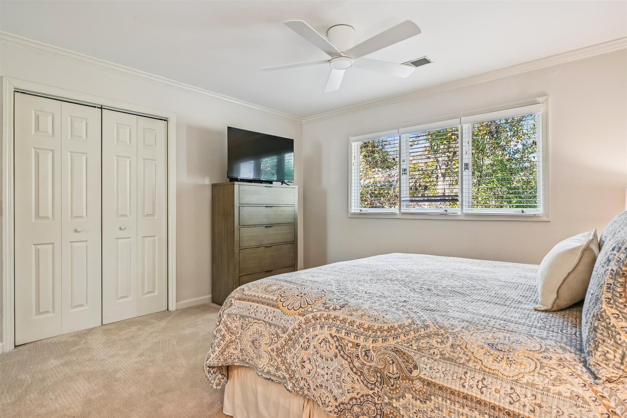 Une chambre à coucher comprenant un lit, un ventilateur de plafond, une armoire et une fenêtre avec des stores.