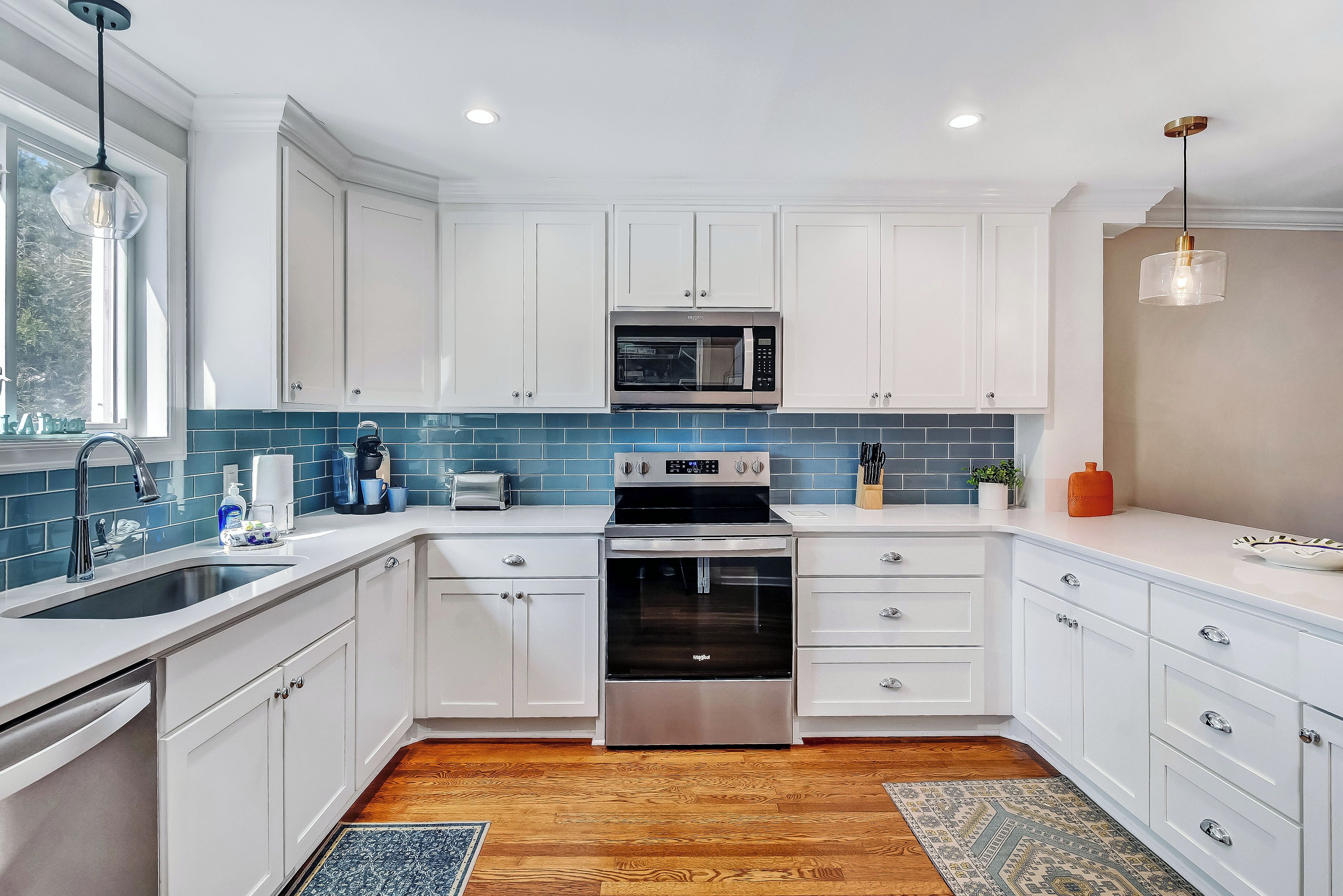 A modern kitchen with white cabinets, a stainless steel oven, a microwave, and a sink with a faucet.