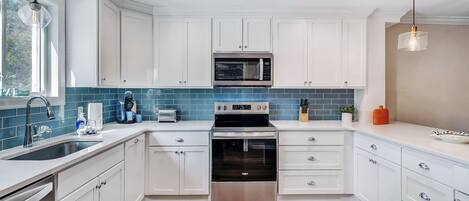 A modern kitchen with white cabinets, a stainless steel oven, a microwave, and a sink with a faucet.
