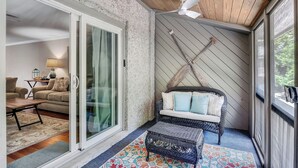 Ein gemütliches Zimmer mit einer Schiebeglastür, die auf einen Balkon führt, mit einem Korbssessel, Kissen, einem kleinen Tisch und einem gemusterten Teppich.