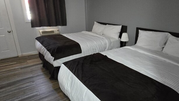 A hotel room with two beds, a bedside table with a lamp, a telephone, and a window with curtains. - Roblin Motor In (Roblin)