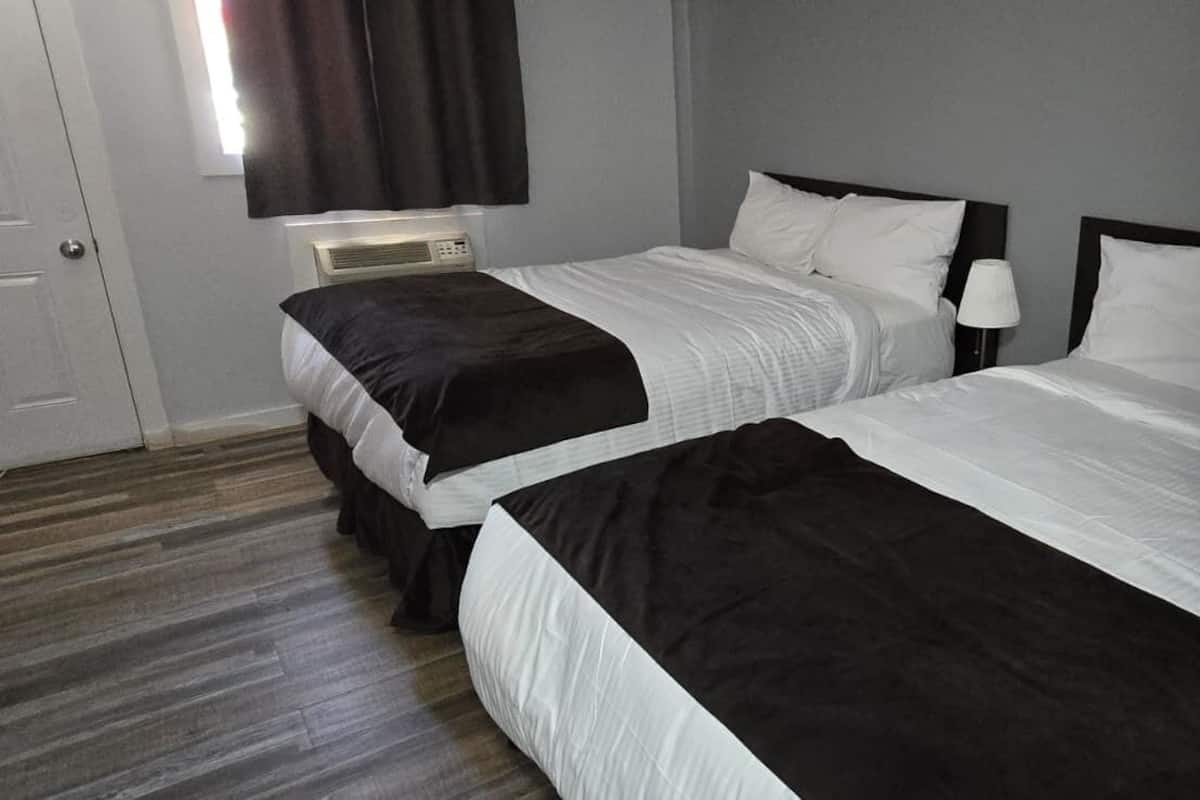 A hotel room with two beds, a bedside table with a lamp, a telephone, and a window with curtains.