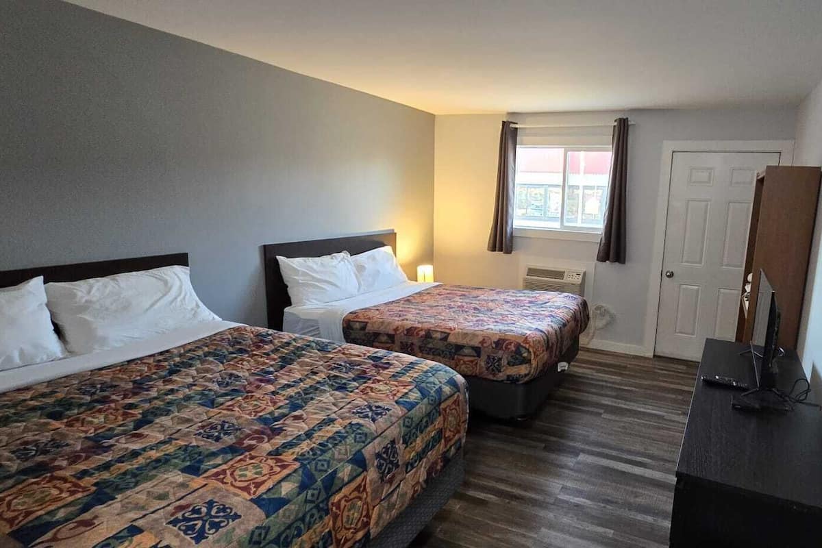 Hotellihuone, jossa on kaksi sänkyä, työpöytä, tuoli, ikkuna, jossa on verhot, ja ovi.